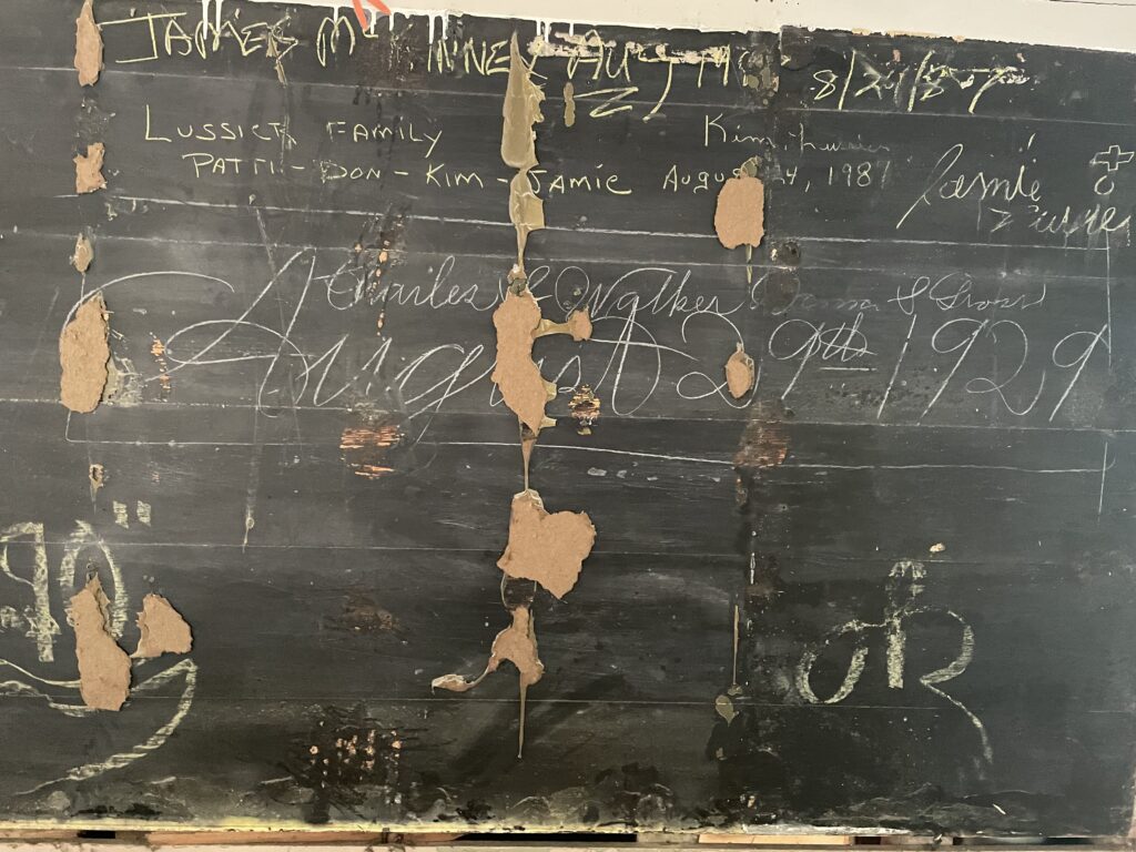 Old, worn blackboard with peeling paint and handwritten notes, representing school history and community.